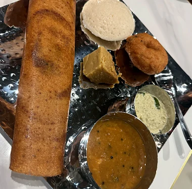 Rolled dosa, idli, vada and a sweet with chutney and sambar on a steel tray